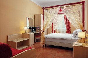 A hotel room with a bed, a desk, a chair, a nightstand, and a bedside table.