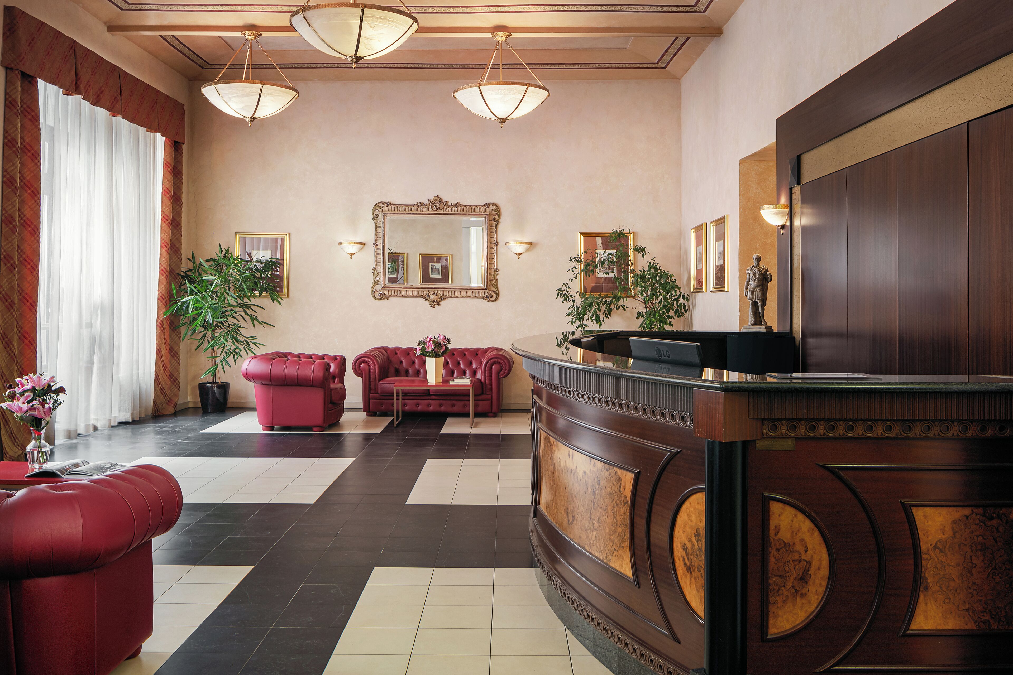 Eine Lobby mit einer Rezeption, roten Sofas, einem großen Spiegel und zwei Zimmerpflanzen.