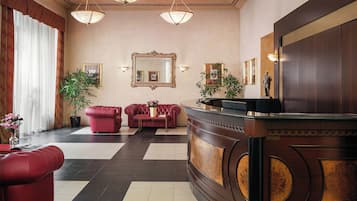 Eine Lobby mit einer Rezeption, roten Sofas, einem großen Spiegel und zwei Zimmerpflanzen.