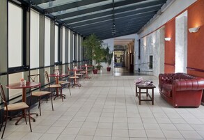 Um espaço interno amplo, com várias mesas e cadeiras, um sofá de couro vermelho e plantas em vasos.