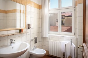 Uma casa de banho com duas pias, um bidé, um porta-toalhas e uma janela com vista para um edifício.