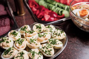 Uma travessa de ovos recheados decorada com cebolinha, uma saladeira e fatias de pepino e tomate em uma bancada escura.