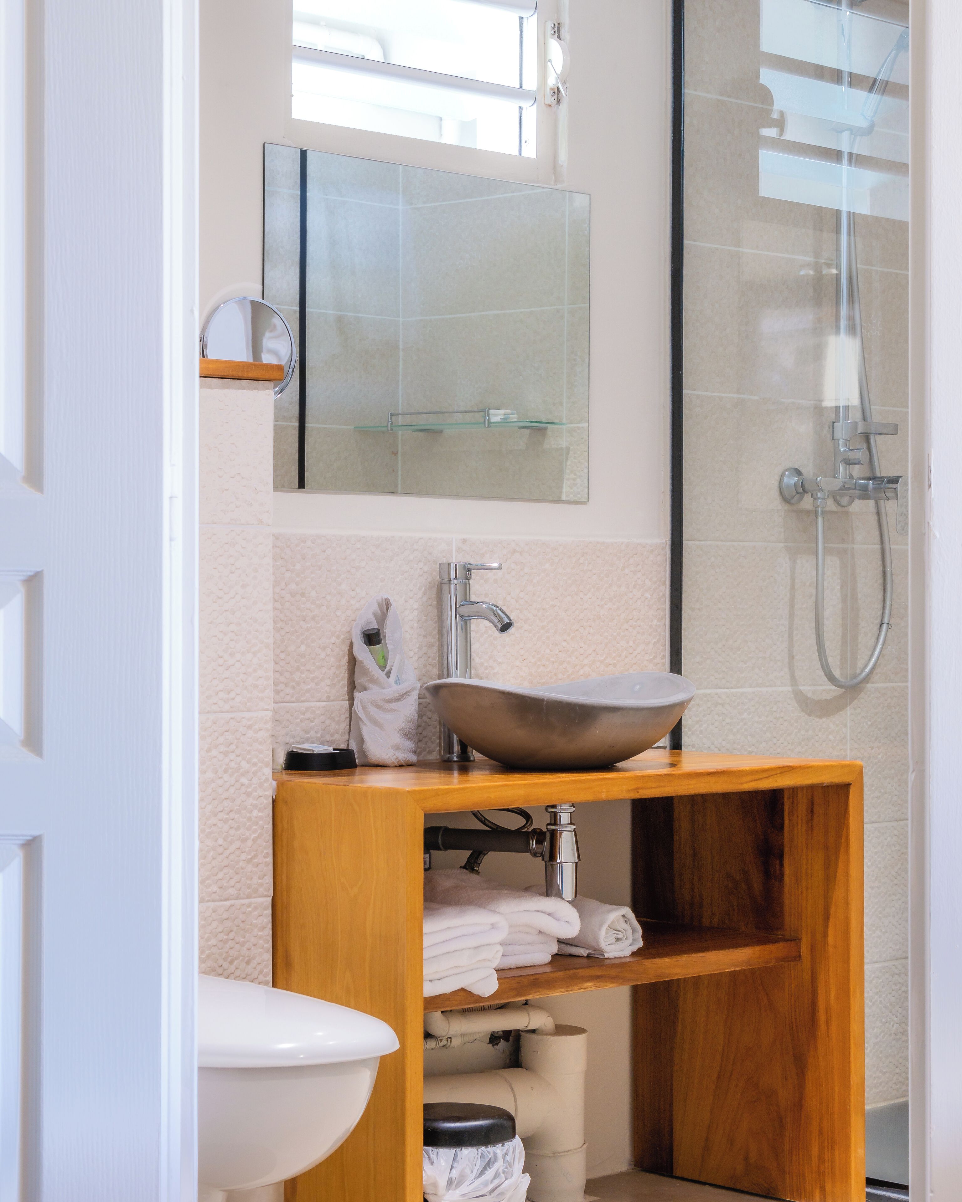 Un baño moderno con tocador de madera, un lavabo sobre encimera, cabina de ducha de vidrio y un espejo grande sobre el lavabo.