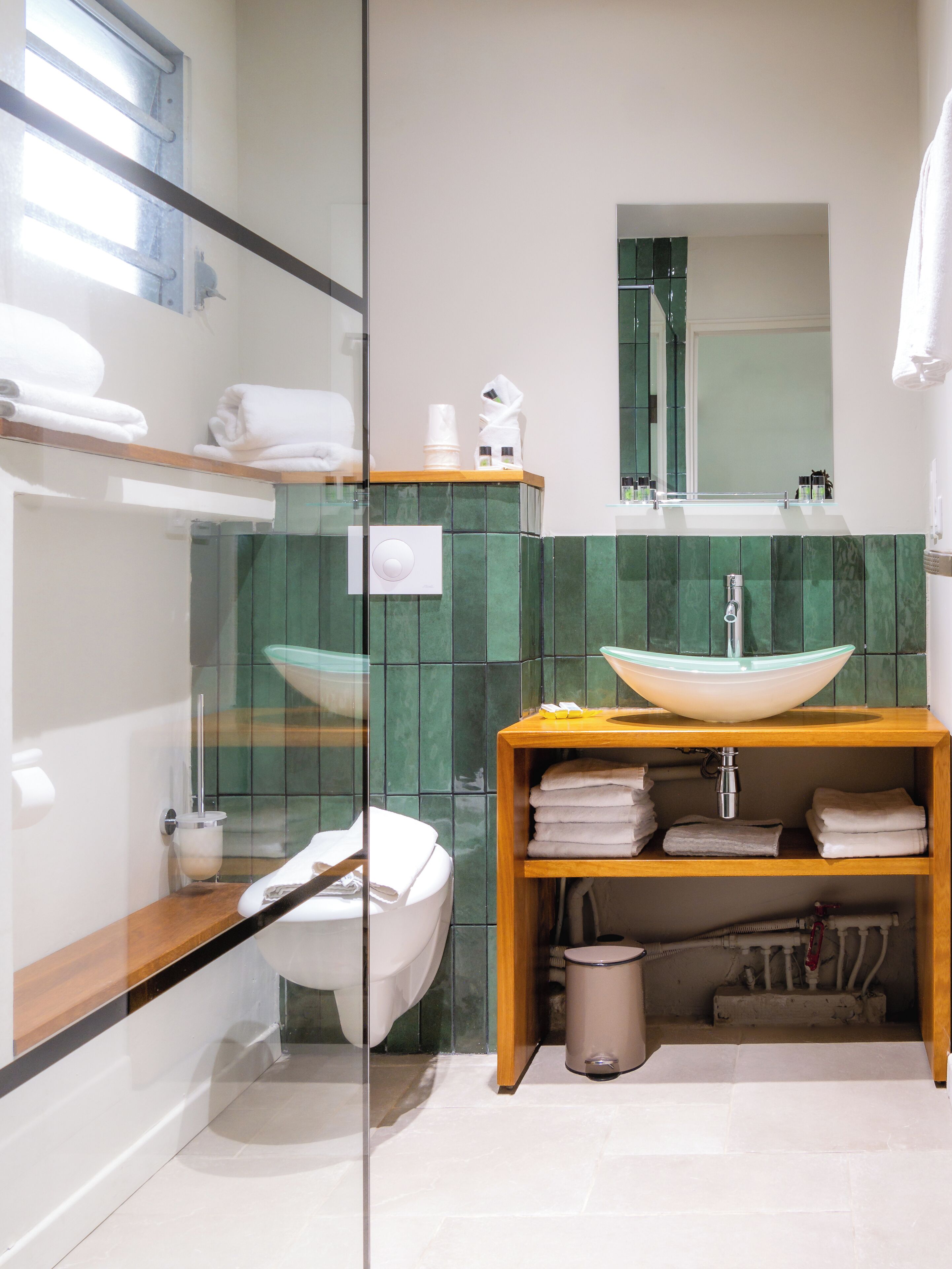 A modern bathroom with a glass shower enclosure, a white toilet, a wooden vanity with a sink, and a mirror above the mirror.