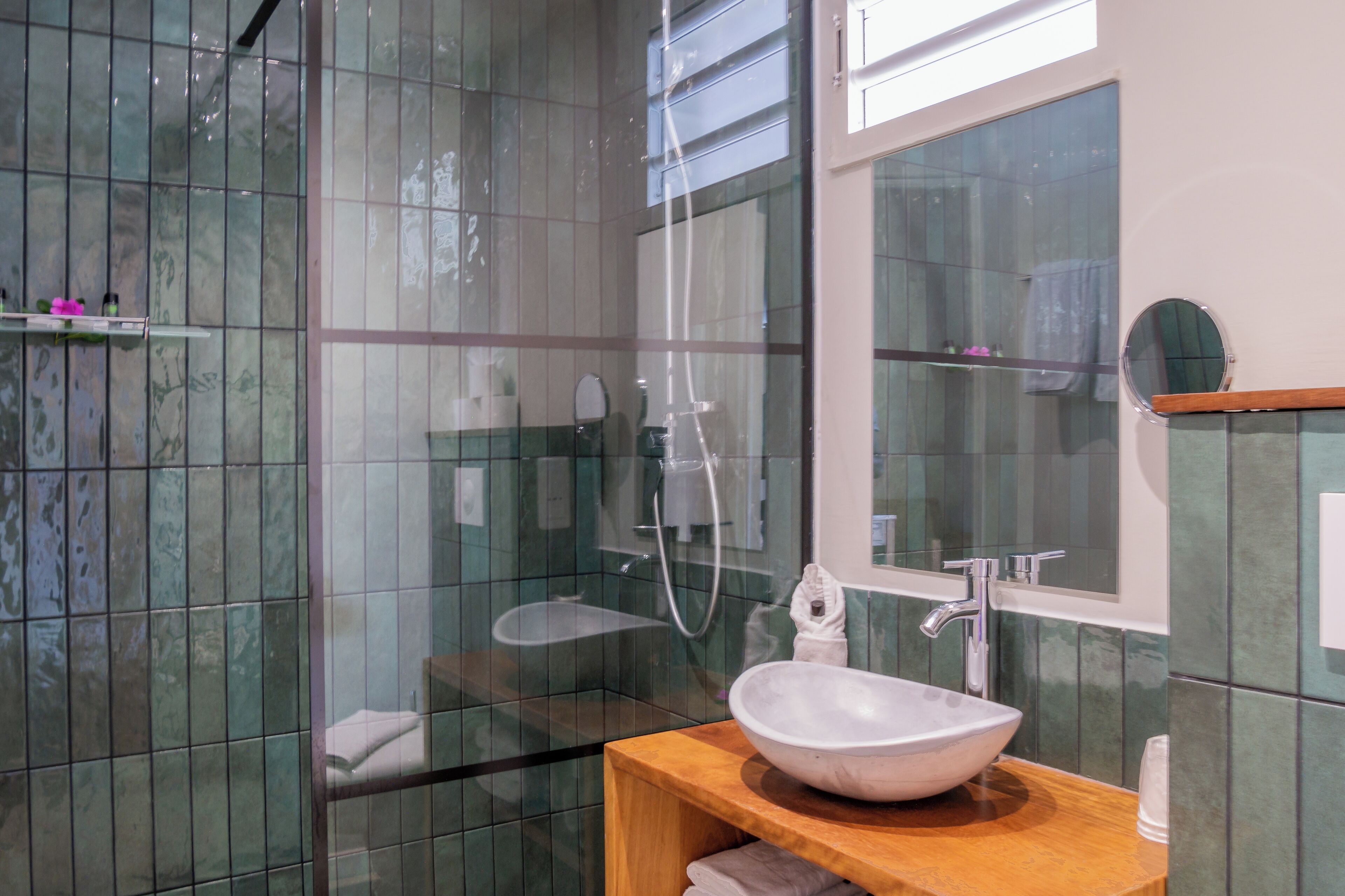 Un baño moderno con cabina de ducha de vidrio, un lavamanos blanco con encimera de madera y un espejo sobre el lavamanos.