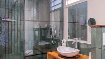 Un baño moderno con cabina de ducha de vidrio, un lavamanos blanco con encimera de madera y un espejo sobre el lavamanos.