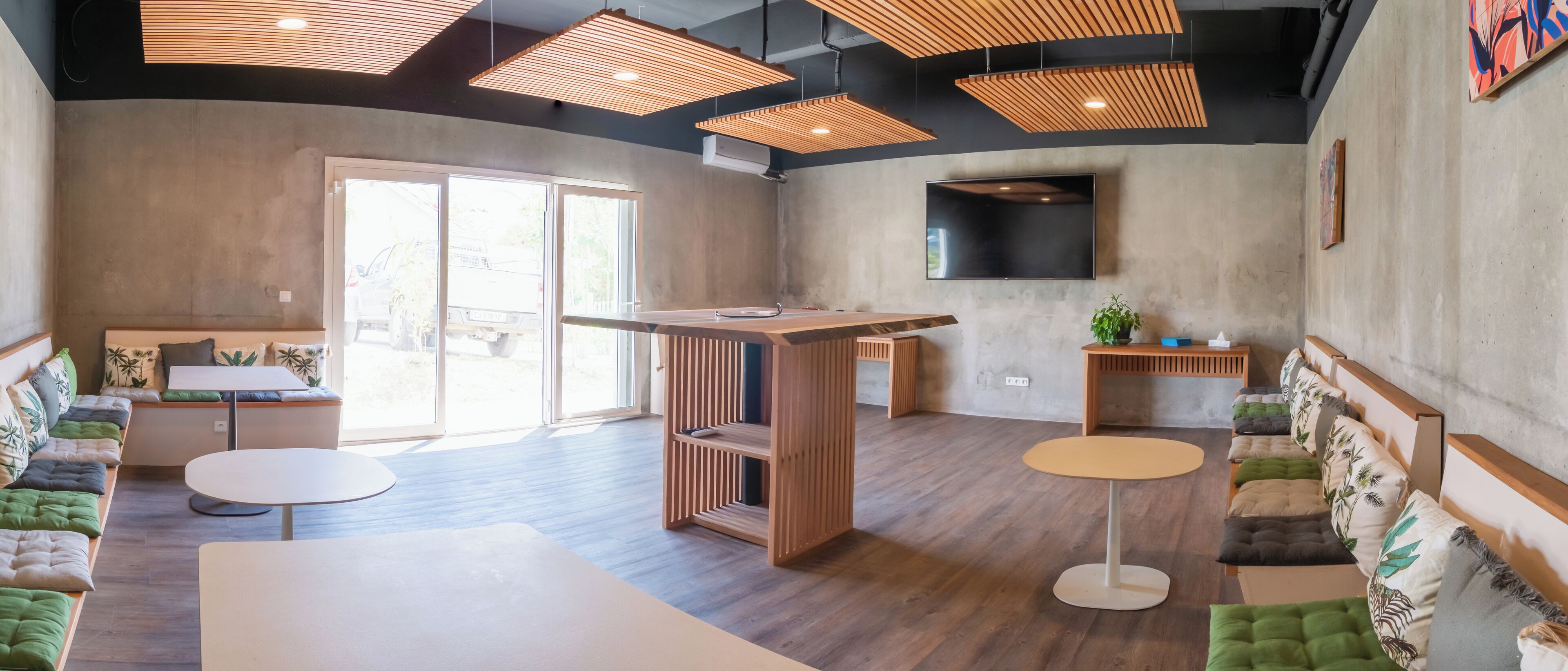 Un intérieur moderne avec un comptoir d’accueil en bois, un espace salon et un téléviseur à écran plat fixé au mur.