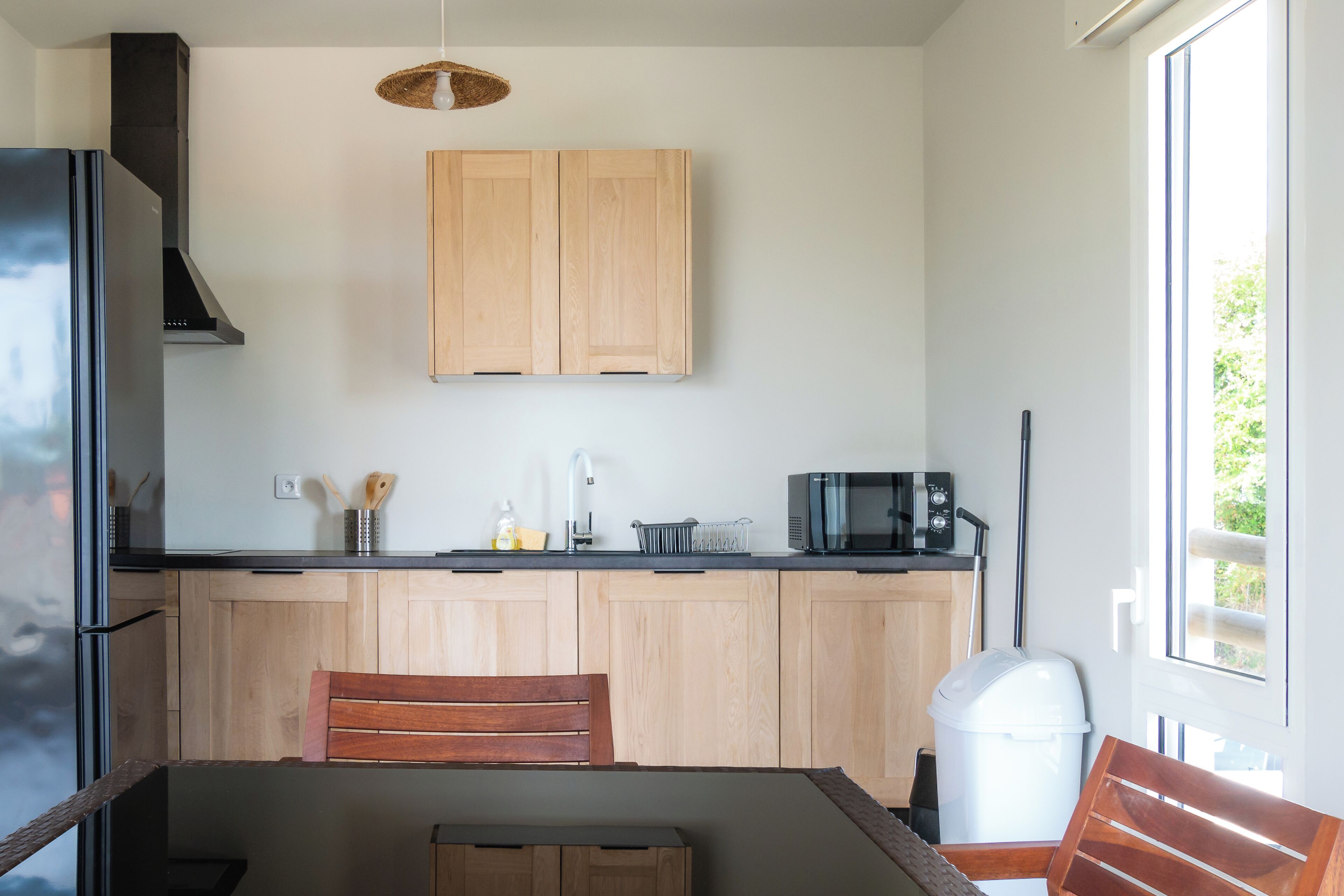 A modern kitchen with wooden cabinets, a black microwave, and a dining area with a wooden table and chairs.