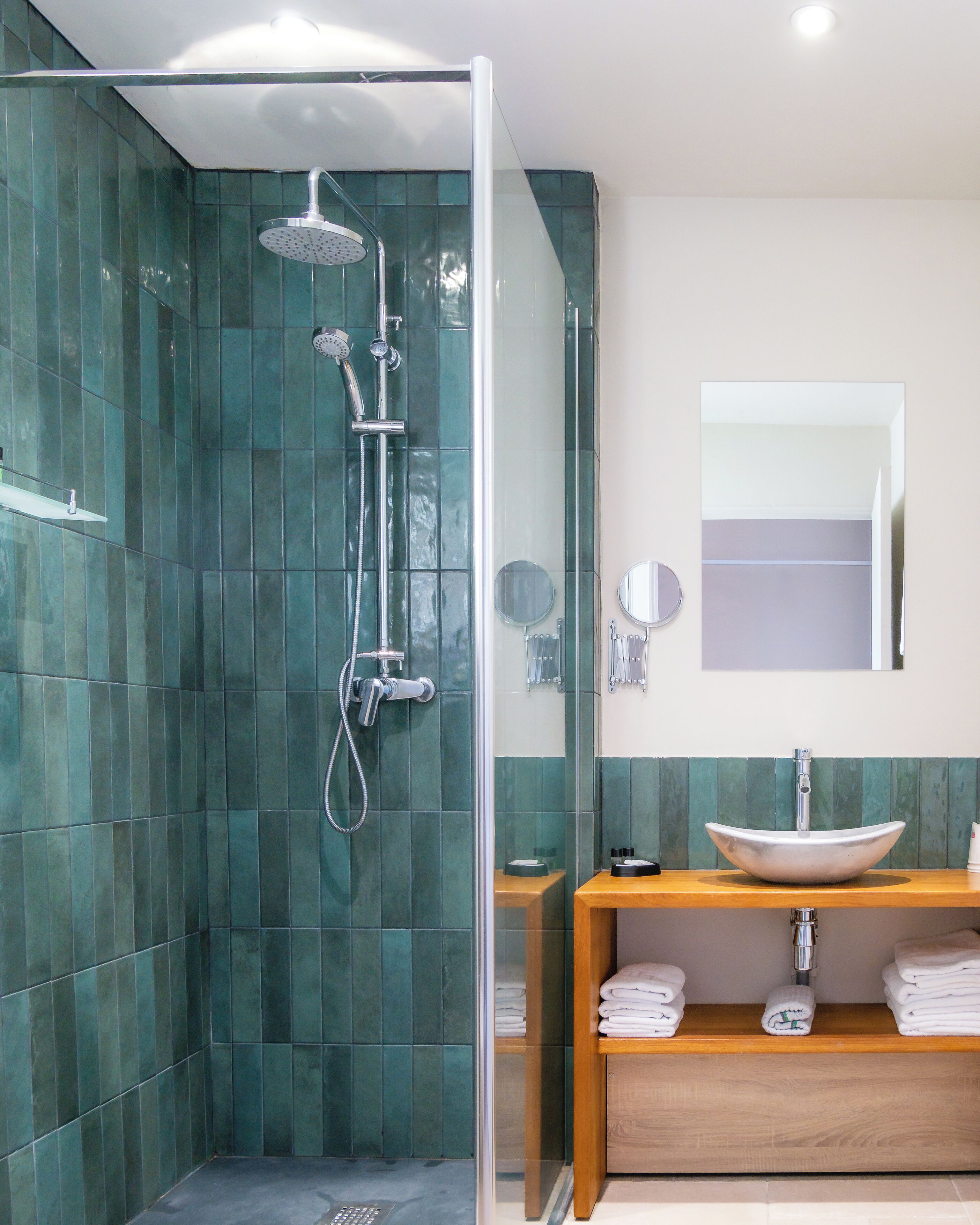 Un baño moderno con ducha envuelta en vidrio, tocador de madera con lavabo y espejo.