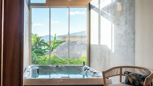 Un baño moderno con un ventanal grande, una bañera de hidromasaje y una silla de mimbre.