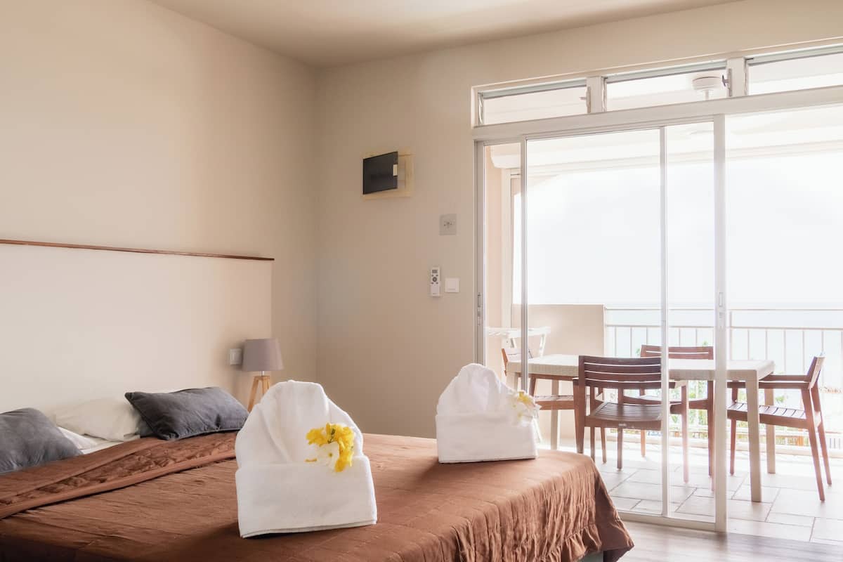 A hotel room with a bed, a balcony with a table and chairs, and a view of the outdoors.