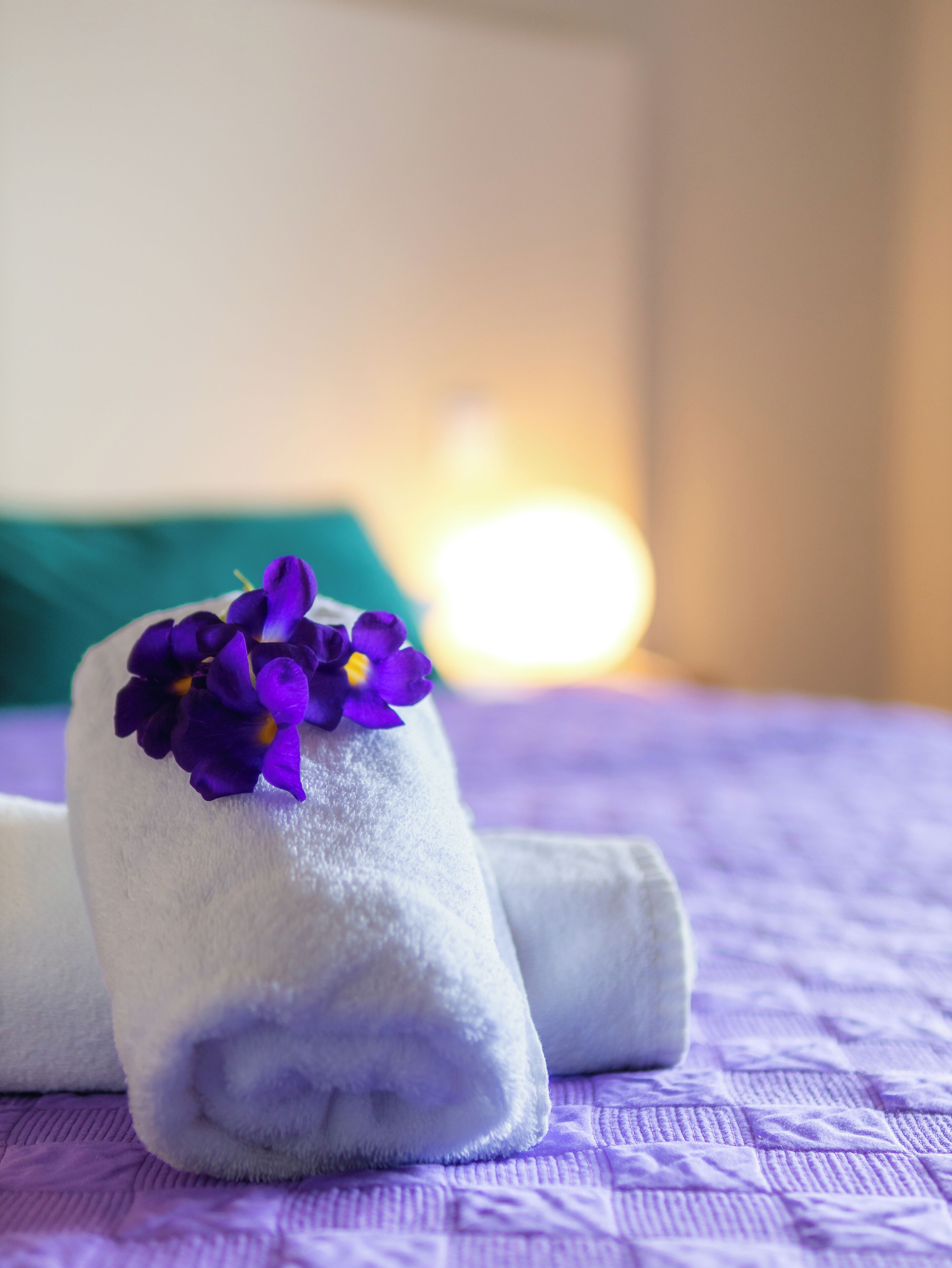 A neatly folded towel with purple flowers on a purple bedspread.