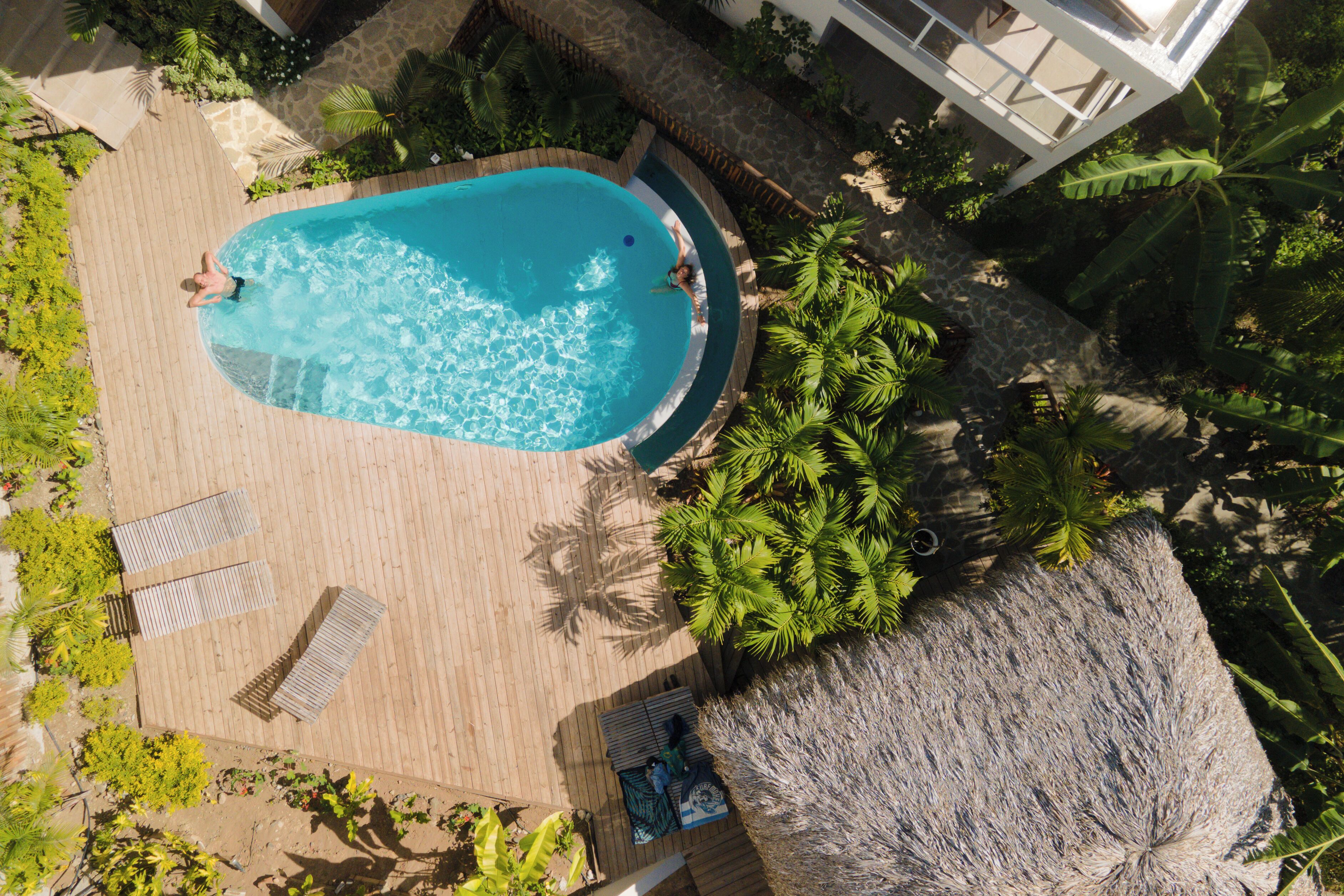 An aerial view of a pool area with a wooden deck, lounge chairs, and tropical plants.