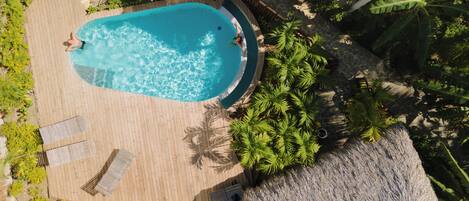 An aerial view of a pool area with a wooden deck, lounge chairs, and tropical plants.