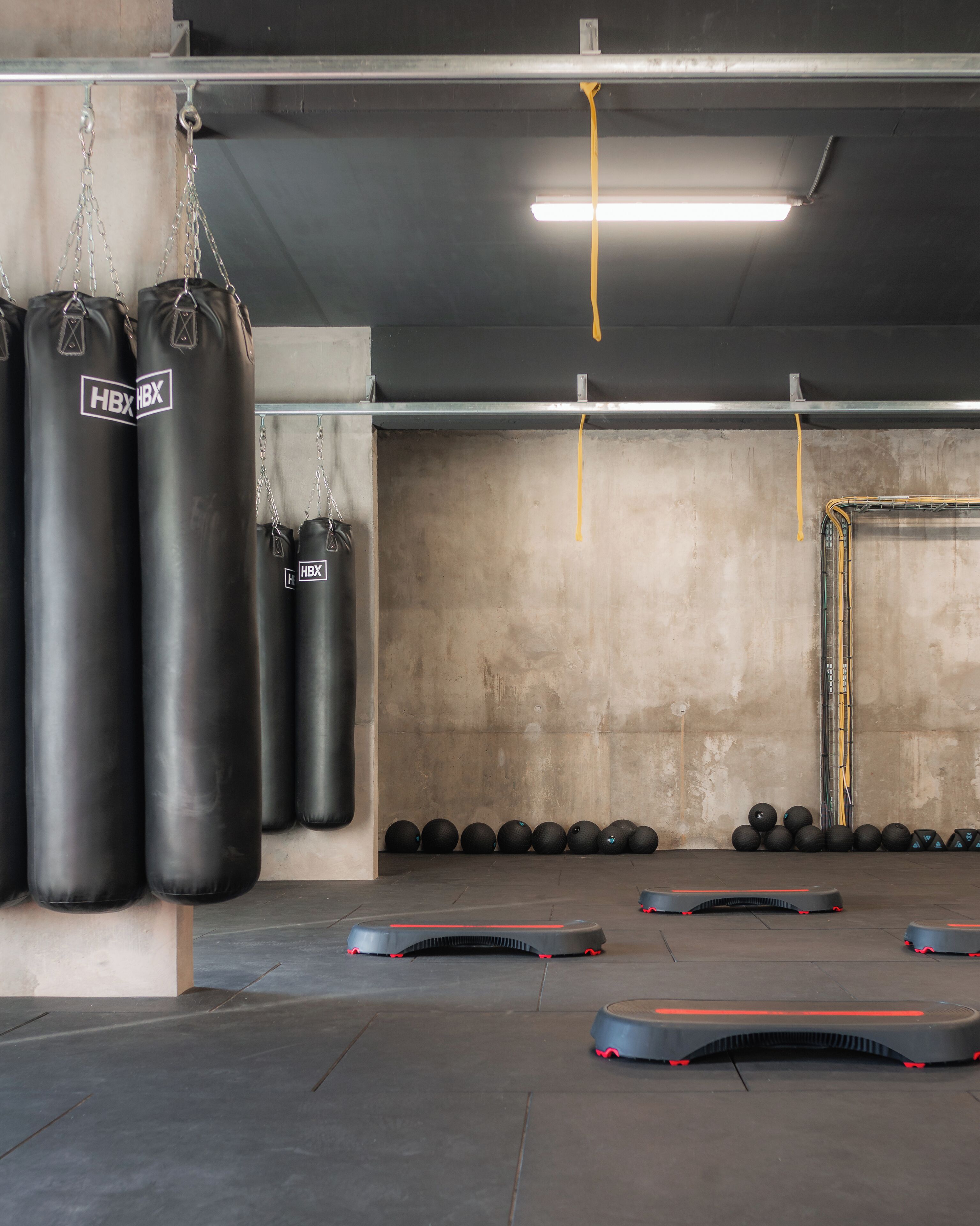 Une salle de sport avec des sacs de frappe noirs, un appareil d’exercice fixé au mur et une rangée de balles lestées.