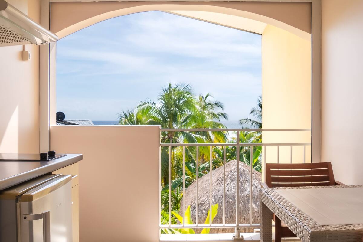 A balcony with a view of palm trees and the ocean.