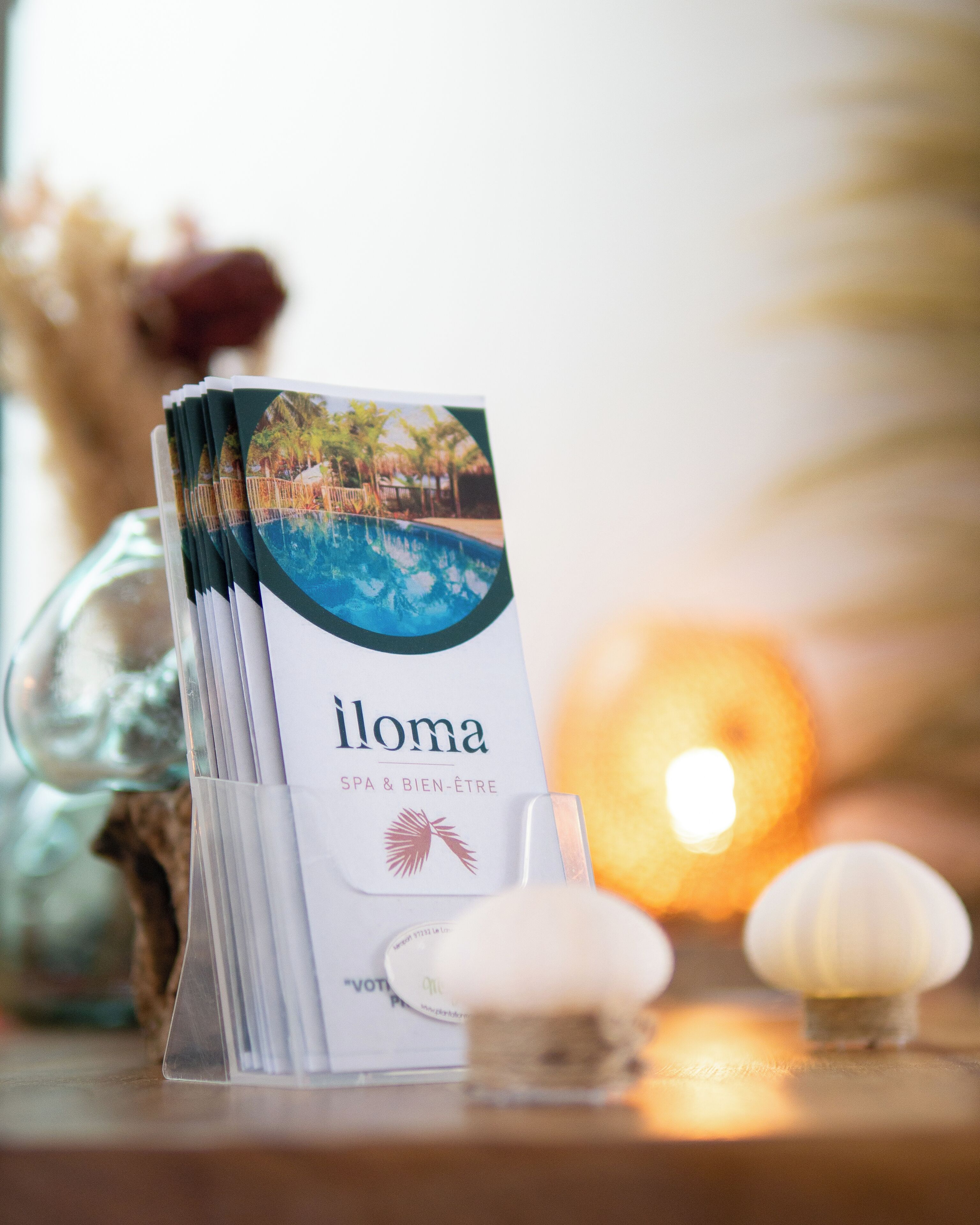 Un montón de folletos para 'iloma SPA & BIEN-ÊTRE' con una piscina y palmeras en la portada.