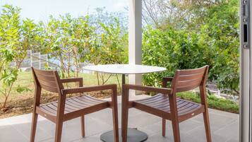 Een terras met twee houten stoelen en een ronde tafel, omringd door groen en een witte schutting.