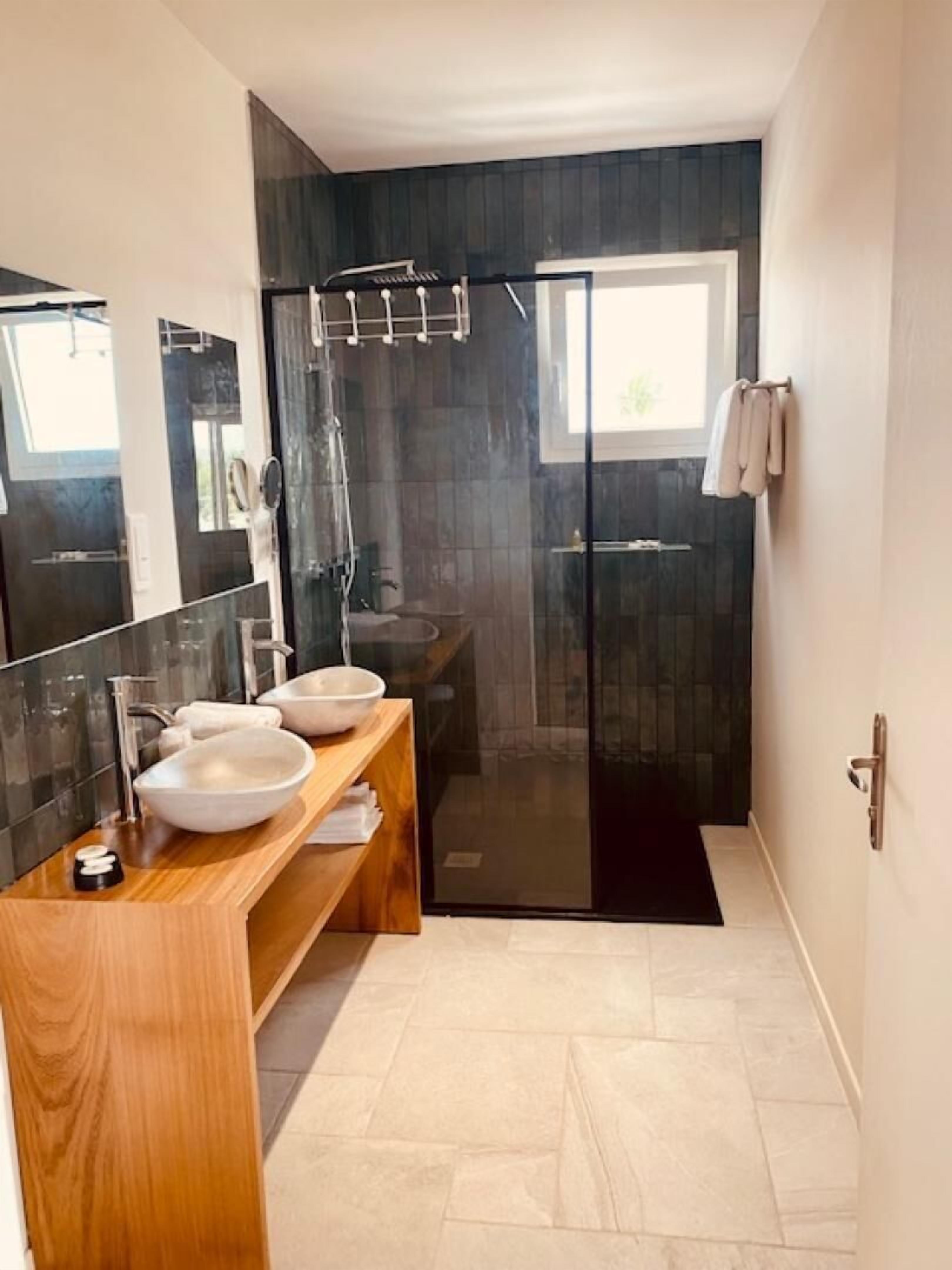 Un baño moderno con dos lavamanos, cabina de ducha de vidrio y un espejo grande.