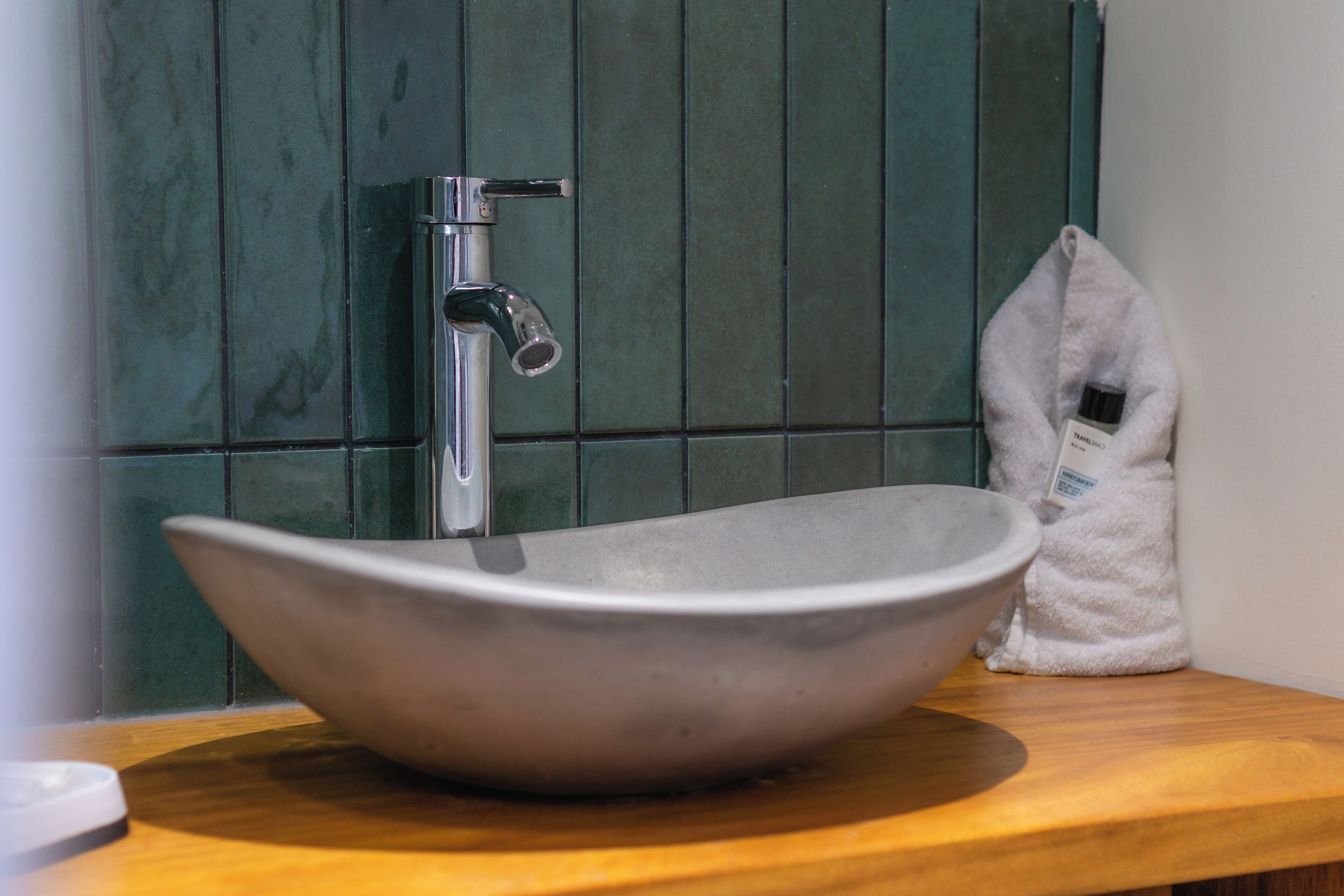 A bathroom with a large, modern vessel sink, a green tiled wall, and a wooden countertop.