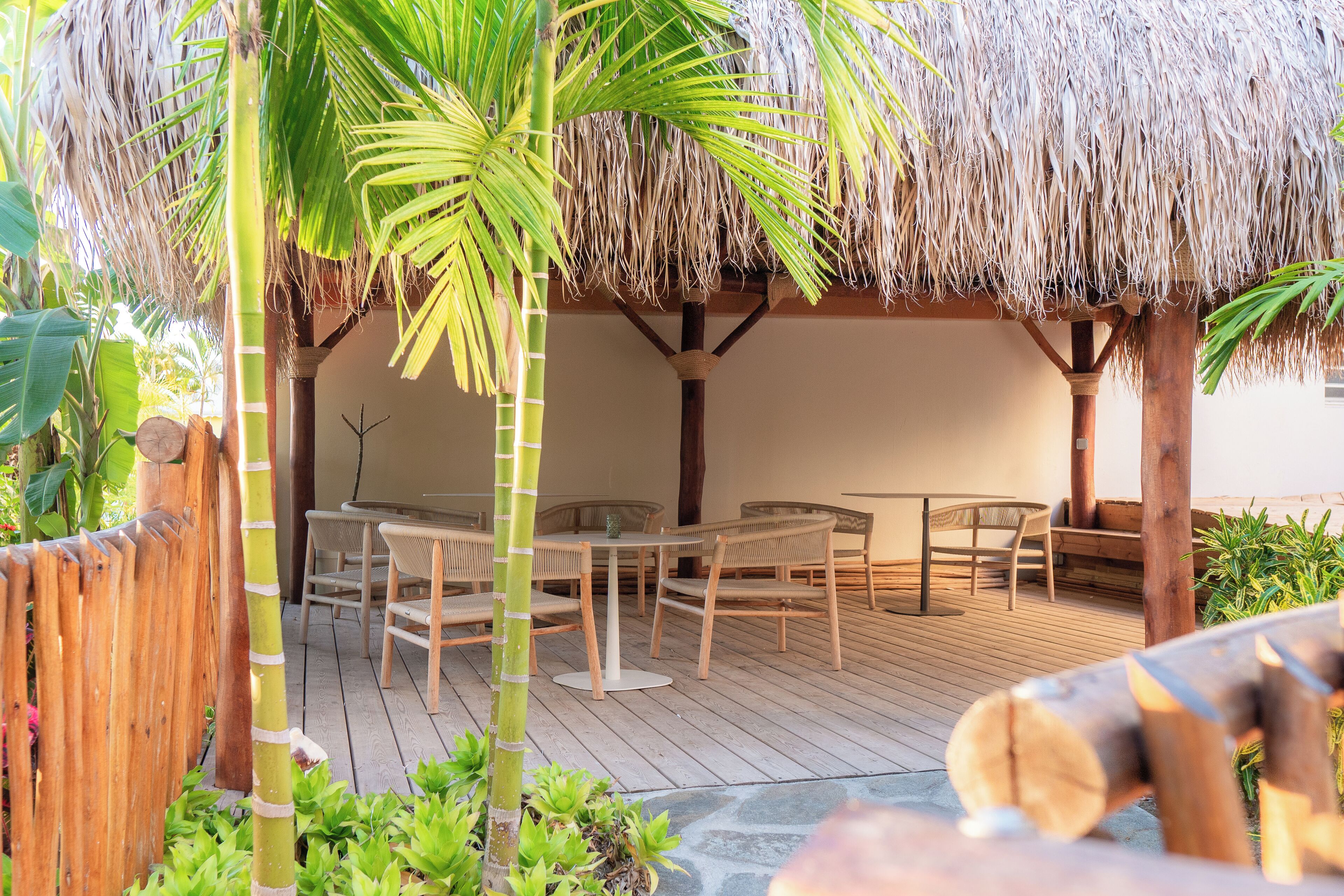 An outdoor patio with thatched roof seating, wooden tables, and chairs.