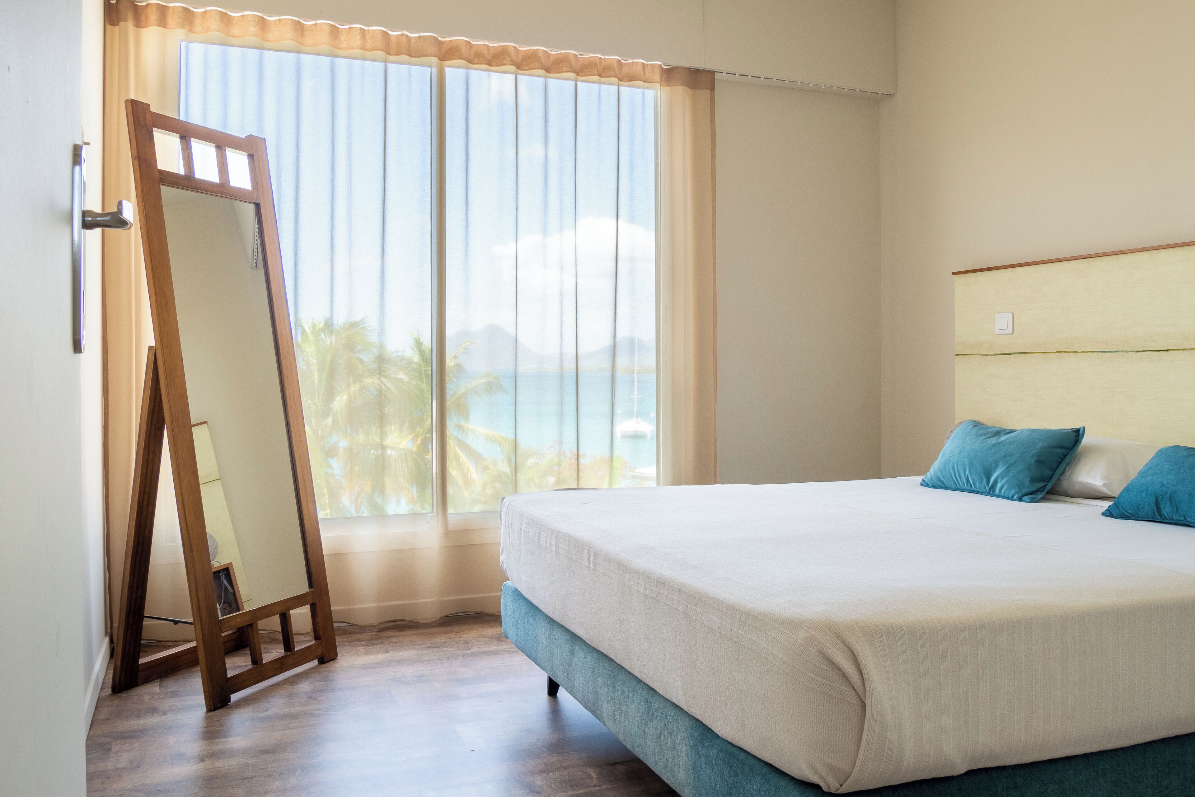 Um quarto com cama, uma janela grande com vista para o mar e uma escada de madeira encostada na parede.