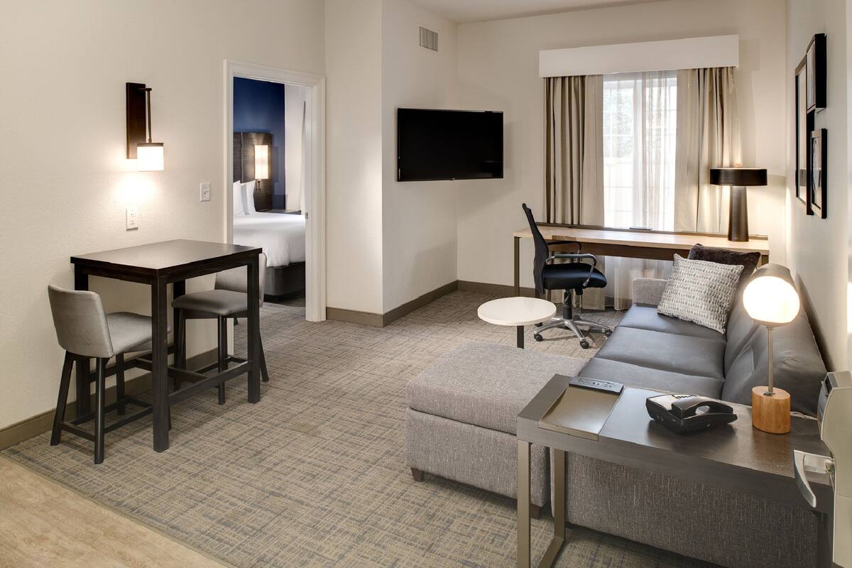 Habitación de hotel con comedor, sofá, televisor y ventana con cortinas.