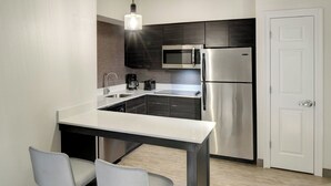 A compact kitchen with a stainless steel refrigerator, microwave, and coffee maker, a white door, and two grey chairs. - Residence Inn by Marriott Columbia Northeast/Fort Jackson Area (Columbia)