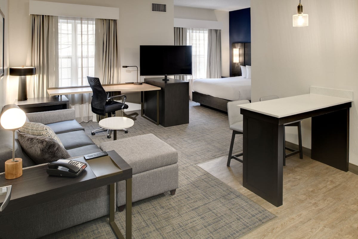 Una habitación de hotel moderna con sofá, escritorio, televisión, cama y una mesita.