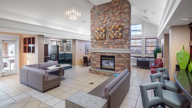 A spacious living area with a stone fireplace, seating arrangements, and a modern kitchen visible in the background. - Residence Inn by Marriott Wichita East at Plazzio (Wichita)