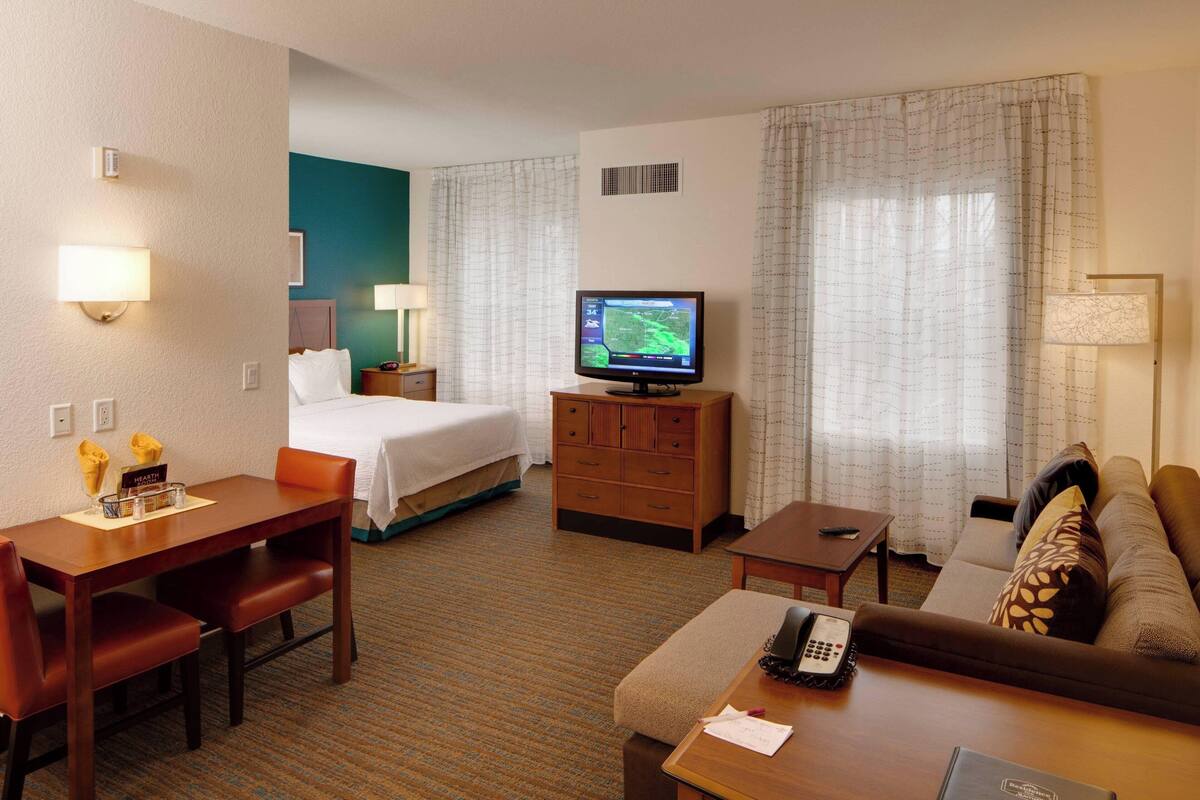 A hotel room with a bed, a TV, a desk with a chair, a sofa, and a small table.