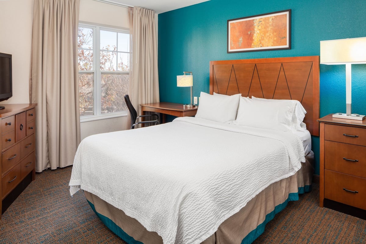 A hotel room with a large bed, a desk, a chair, a TV, and a window with curtains.