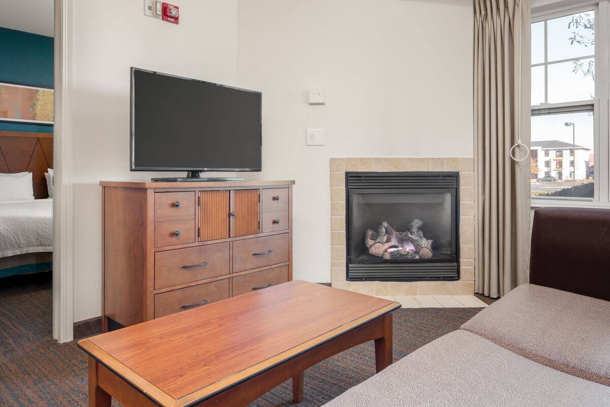 A hotel room with a television, a fireplace, a sofa, and a wooden table.