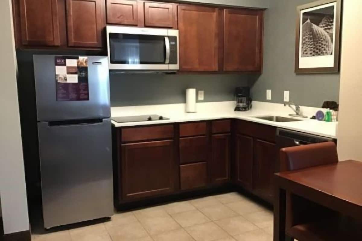 A compact kitchen with wooden cabinets, a stainless steel refrigerator, a microwave, and a sink.
