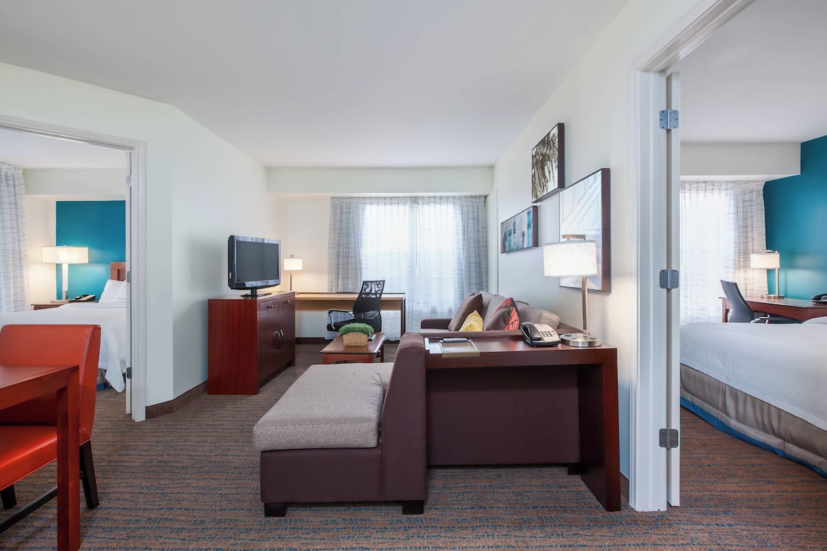 A hotel room with a bed, a desk with a computer, a TV, a sofa, and a chair.
