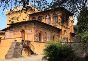 Un edificio histórico con un patio central, una escalera que conduce a la entrada y una pequeña zona ajardinada.