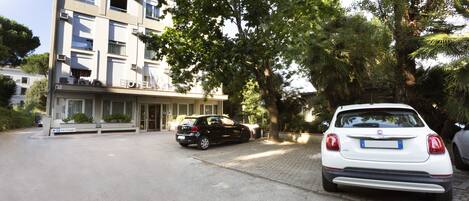 A hotel with a parking area, a black car, and a white car parked in front.