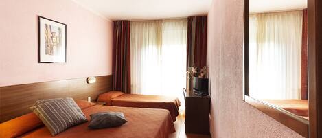 A hotel room with two beds, a TV, and a window with curtains.