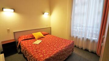 A hotel room with a bed, two bedside lamps, a window with curtains, and a nightstand.