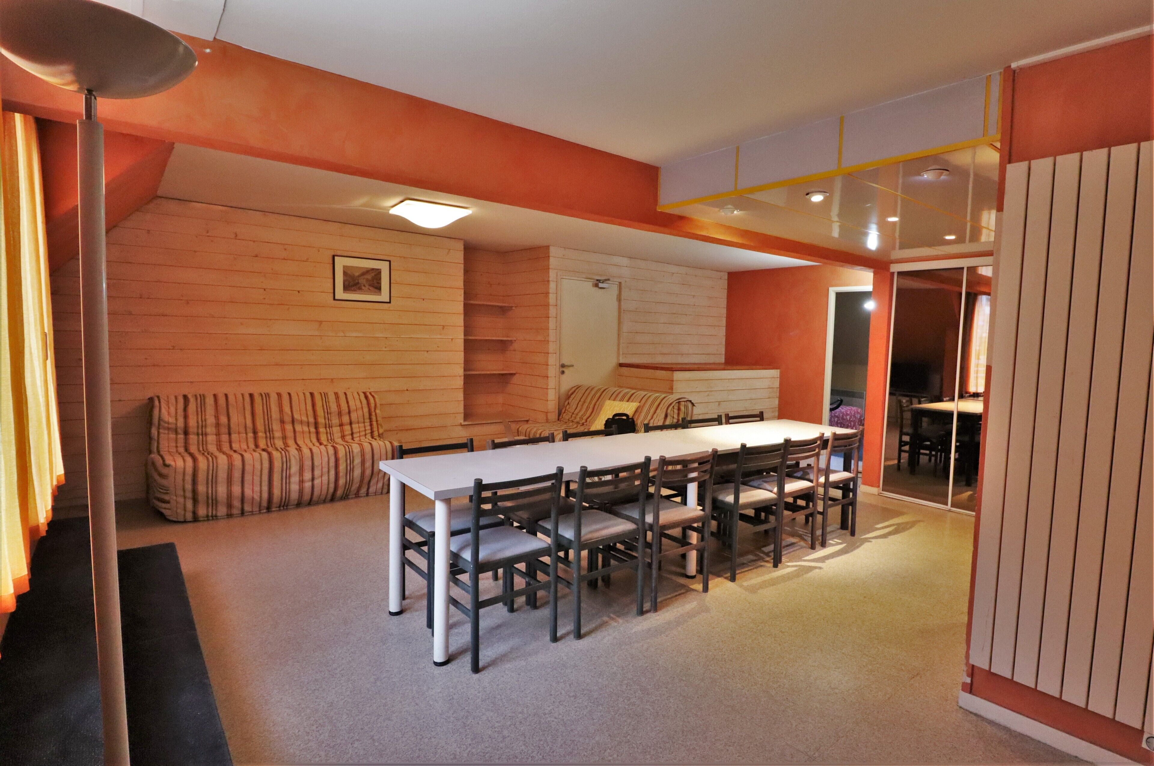 A dining area with a long table and chairs, a sofa, and a ceiling light fixture.