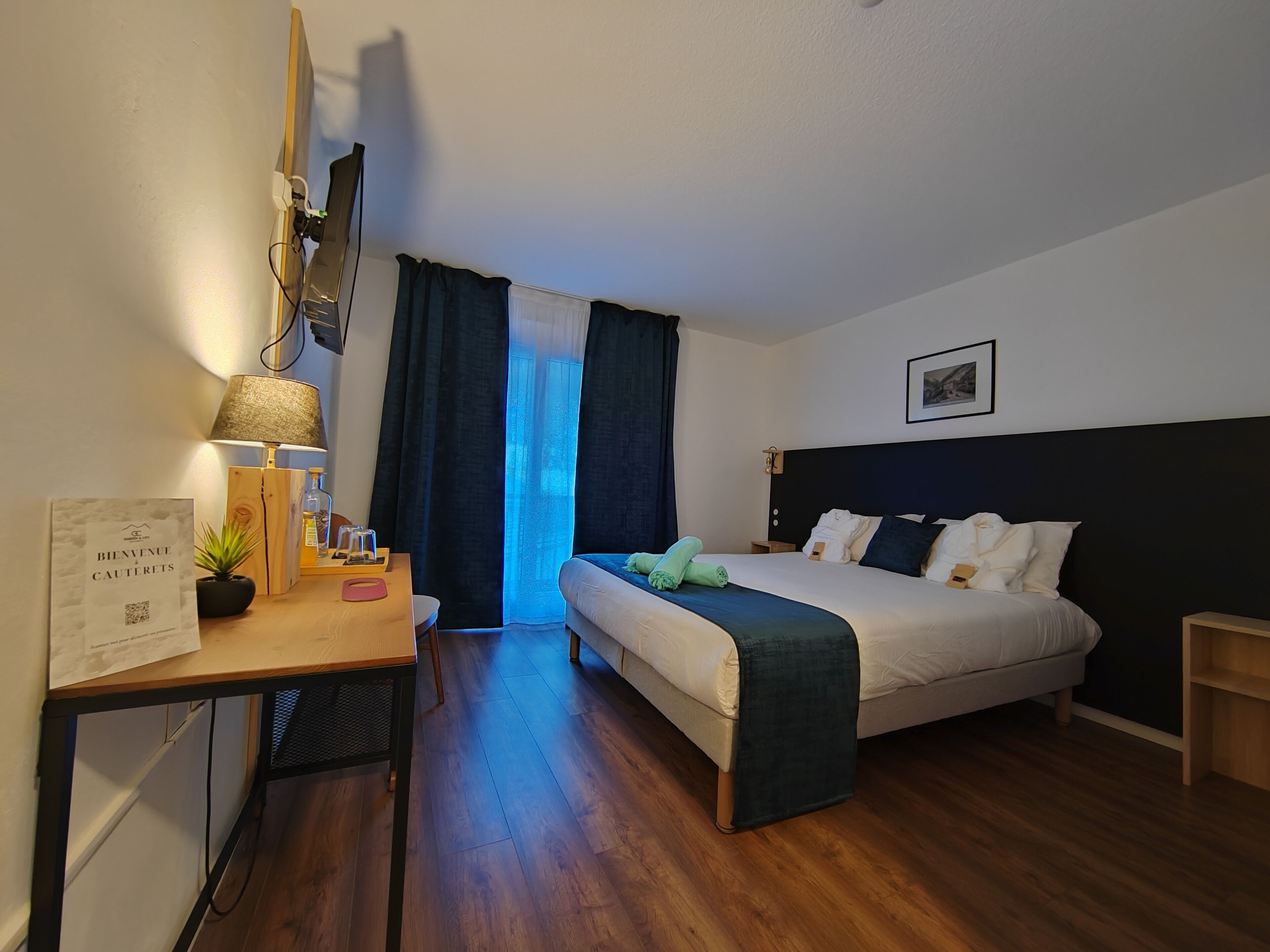 A hotel room with a bed, bedside table, lamp, and a desk with a chair.