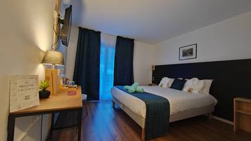 A hotel room with a bed, bedside table, lamp, and a desk with a chair.