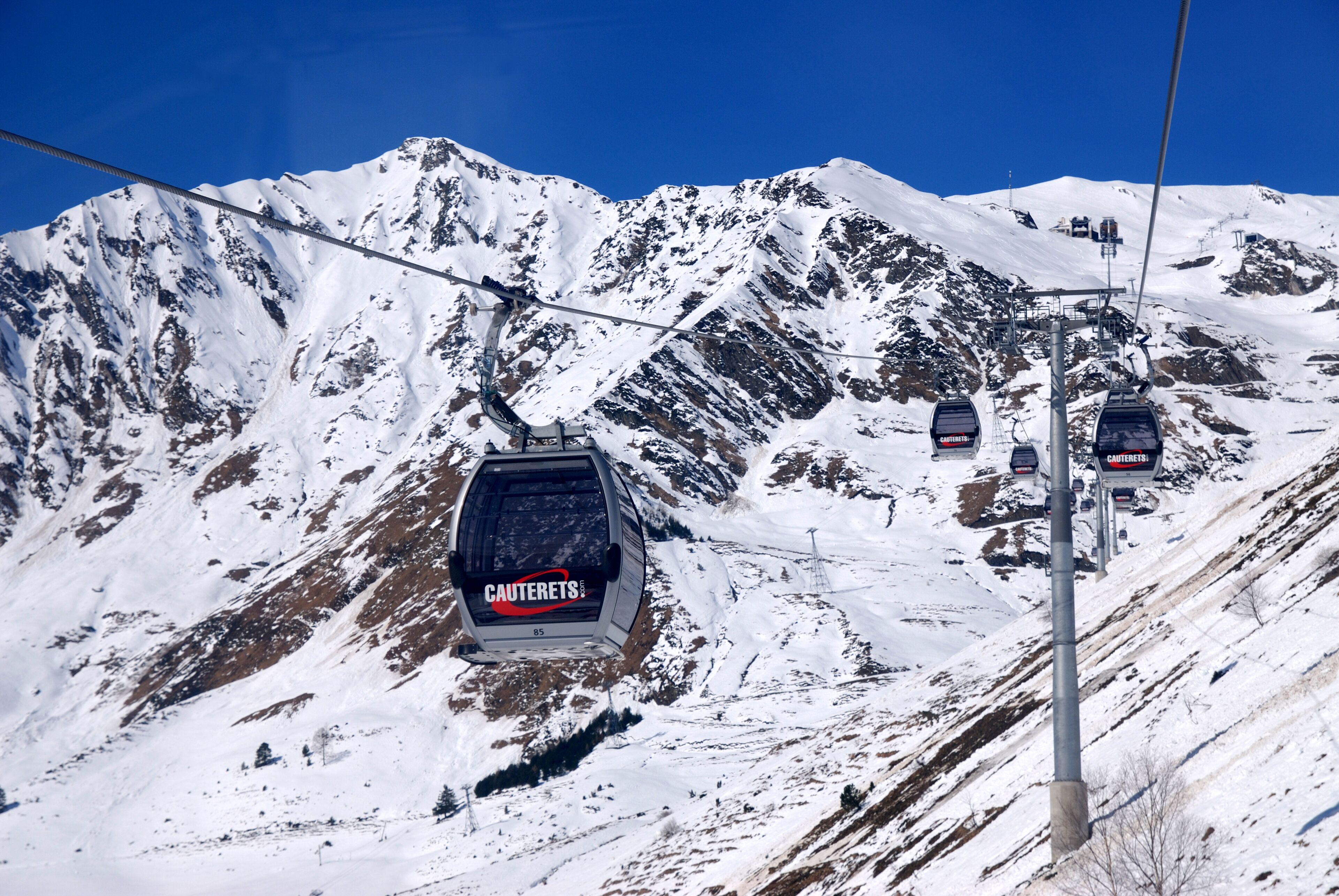 Eine Sesselbahn mit dem Schriftzug 'CAUTERETS' fährt einen verschneiten Berg hinauf.