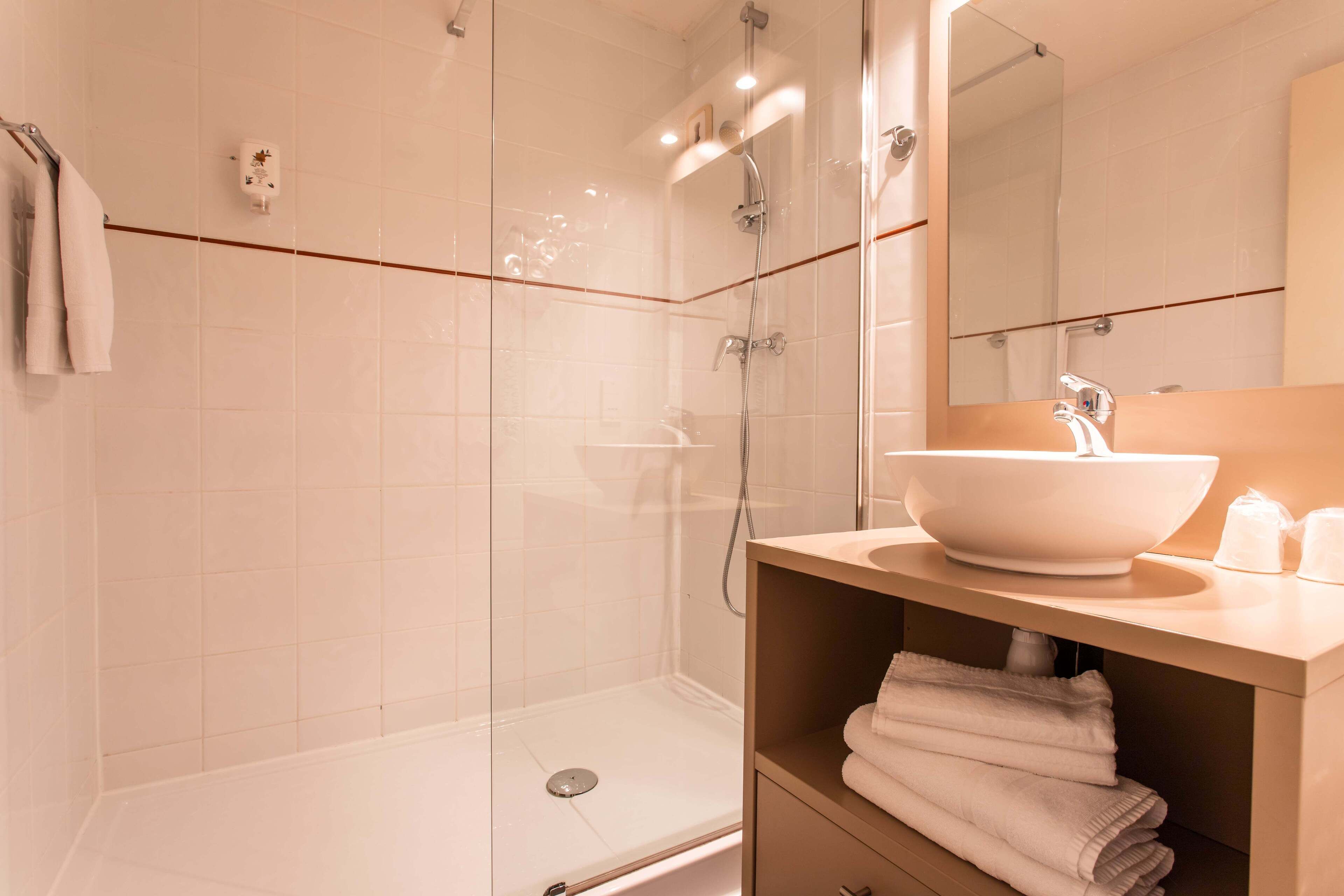 Un baño moderno con ducha de vidrio, un lavabo blanco y un espejo encima.