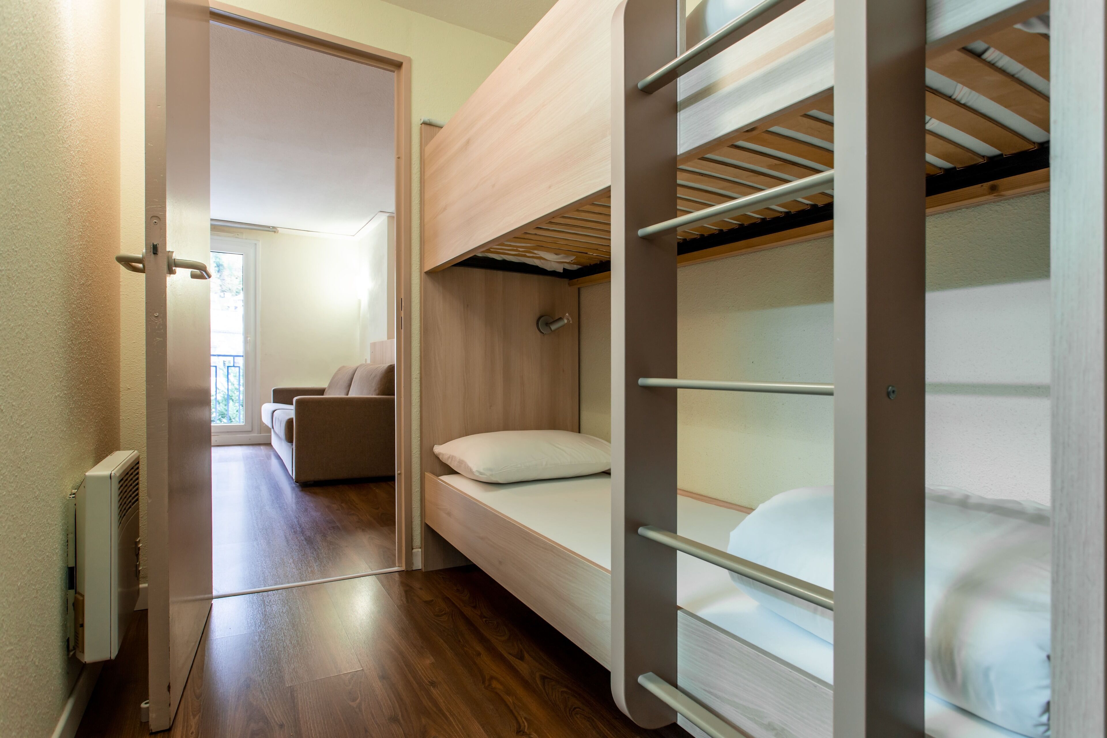 A compact room with a bunk bed, a sofa, and a radiator.