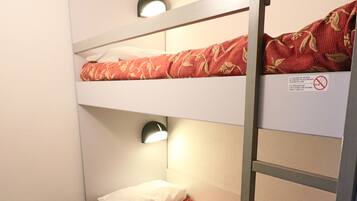 A bunk bed with a red floral bedspread, a small desk with a chair, and a wall-mounted light.