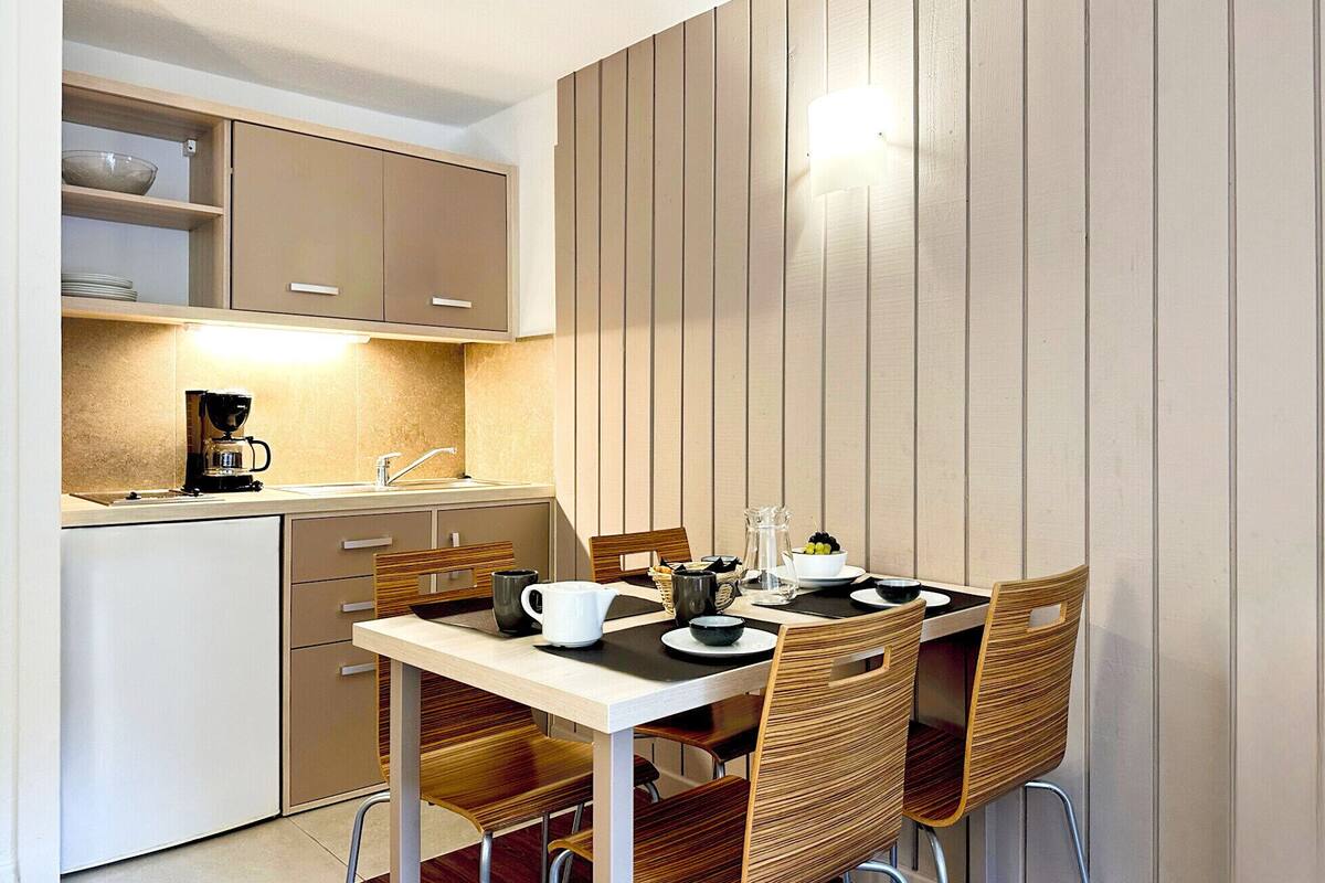 A compact kitchen with a dining area, including a coffee maker, a sink, and wooden chairs.