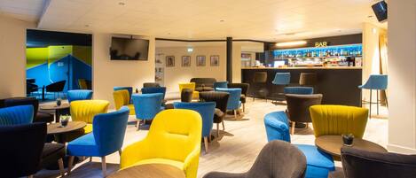 Un espace lounge moderne doté d’un bar, de sièges confortables et d’un téléviseur à écran plat fixé au mur.