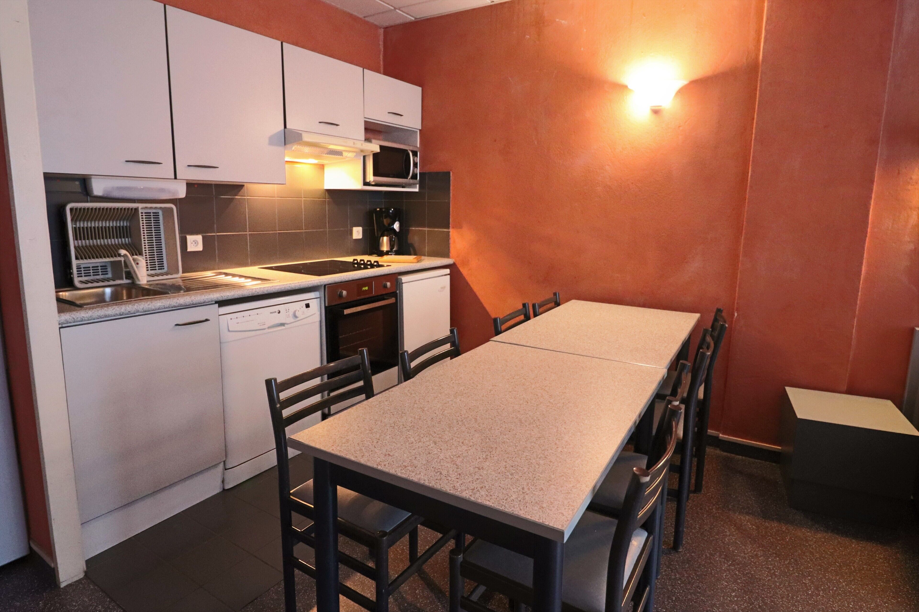 A compact kitchen with white appliances, a dining table, and chairs.