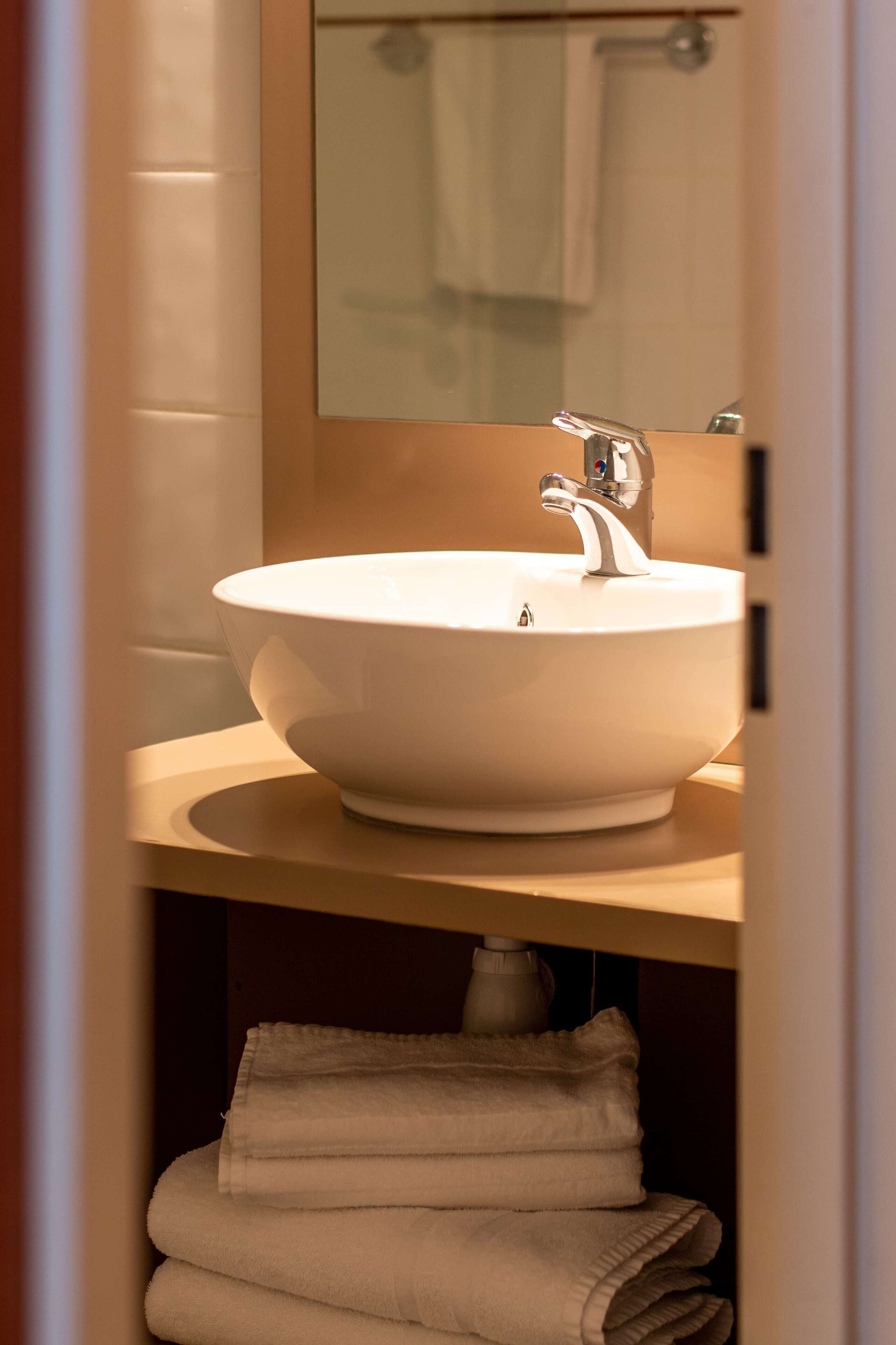 Un baño con un lavamanos blanco, un espejo y un perchero para toallas.